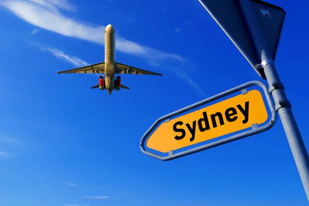 Aeroplane flying above a road sign displaying Sydney