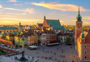 Aerial view of Castle Square in Warsaw’s Old Town at sunset, showing colourful historic buildings and the Royal Castle tower under a golden sky.
