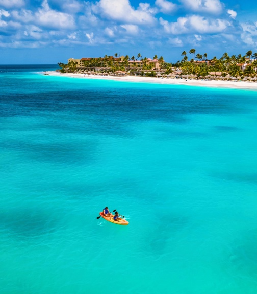 A mid-aged couple paddles together in their kayak, embracing the serenity of Aruba crystalline waters.